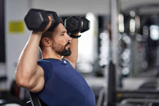Man doing shoulder workout with dumbbells in TriFit gym